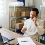 Latin,Entrepreneur,Multitasking,In,His,Small,Business,Warehouse:,Sipping,Coffee,