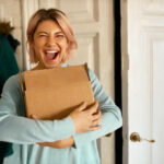 Indoor,Image,Of,Happy,Cheerful,Young,Woman,Holding,Cardboard,Box